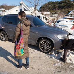 Kyung-ah's husband, Jong-ki, scraping snow from the car in preparation for the trip up to the punchbowl.